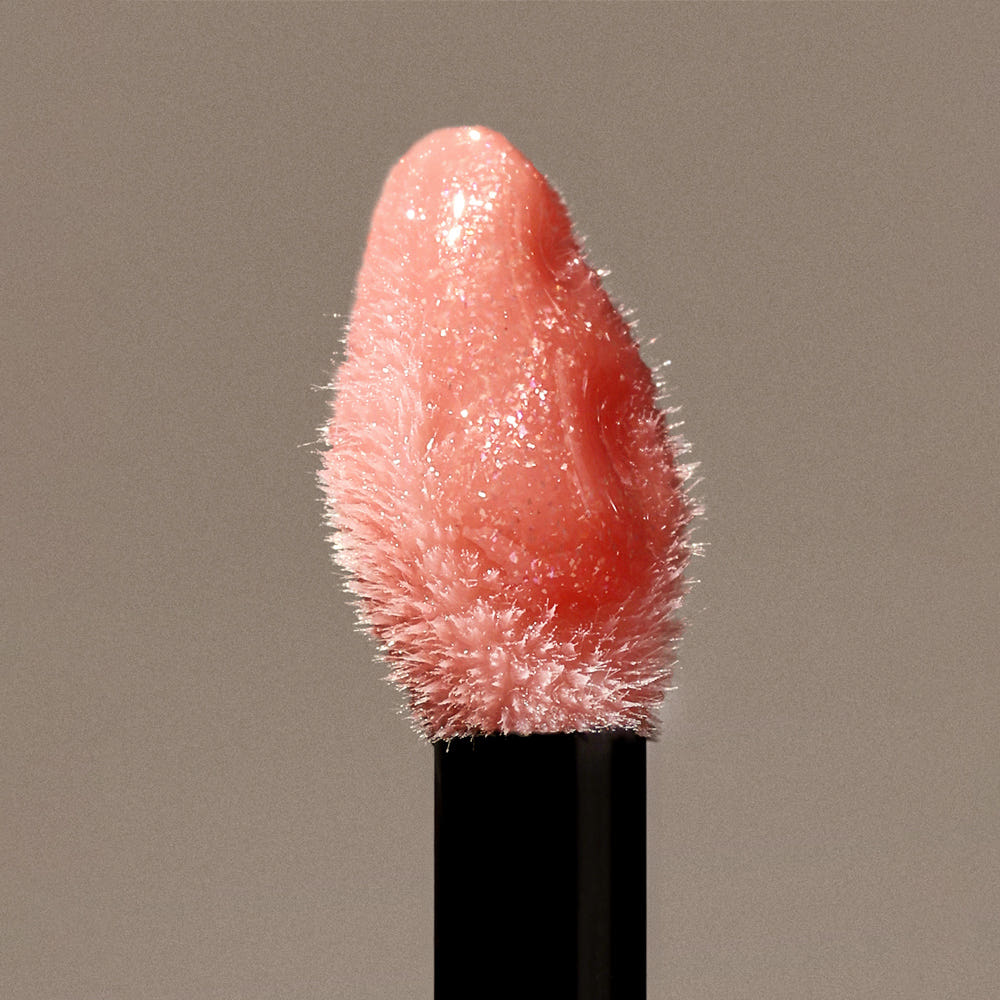 HERA  Sensual Nude Gloss 5g, rouge à lèvres brillant nude, gros plan sur le tube noir sur fond beige, éclairage doux.