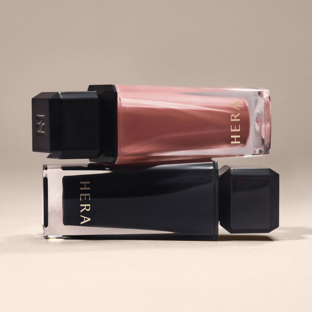 HERA  Sensual Nude Gloss 5g, marque HERA, gloss nude en tube transparent sur fond beige, prise de vue produit.