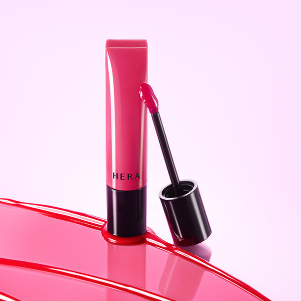 Décris l'image en français en mentionnant le produit, la marque et le contexte visuel. HERA Sensual Tinted Shine Lip Serum 8.5g sur fond rose.