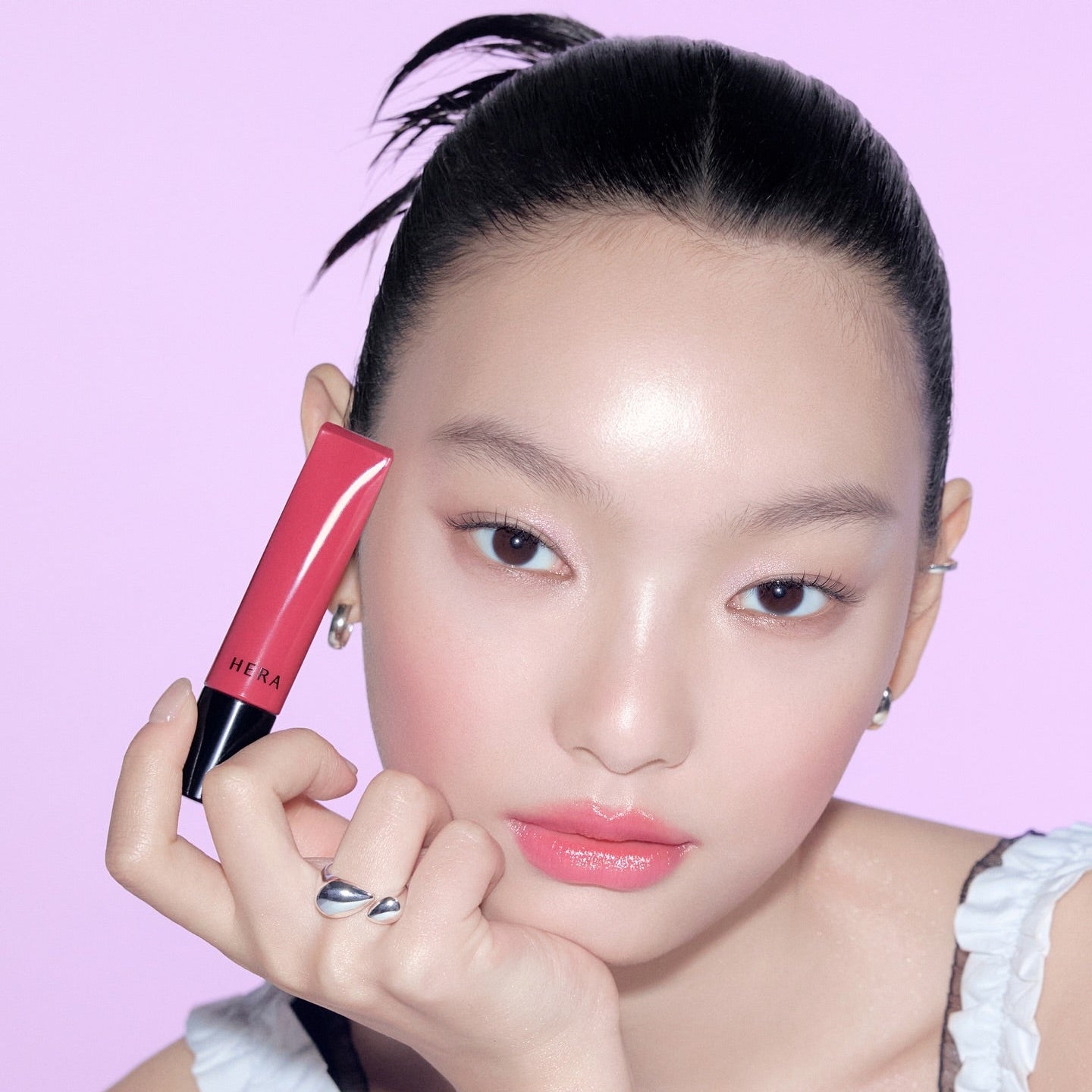 HERA Sensual Tinted Shine Lip Serum 8.5g de HERA, flacon rose tenu par un mannequin sur fond violet.