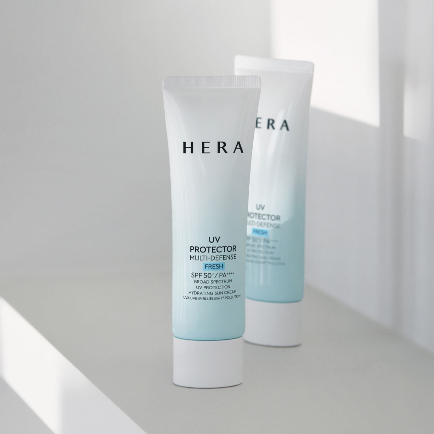 HERA UV Protector Multi-Defense Fresh SPF50+PA++++ 50ml, tubes crème solaire HERA en décor lumineux, fond clair, intérieur.