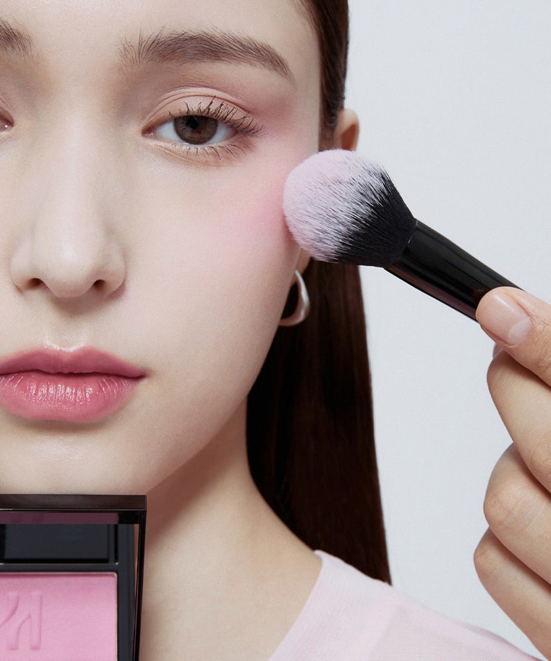 HERA Hera Blush 5.5g utilisé sur une jeune femme, ajoutant une teinte rose délicate à ses joues avec un pinceau doux.