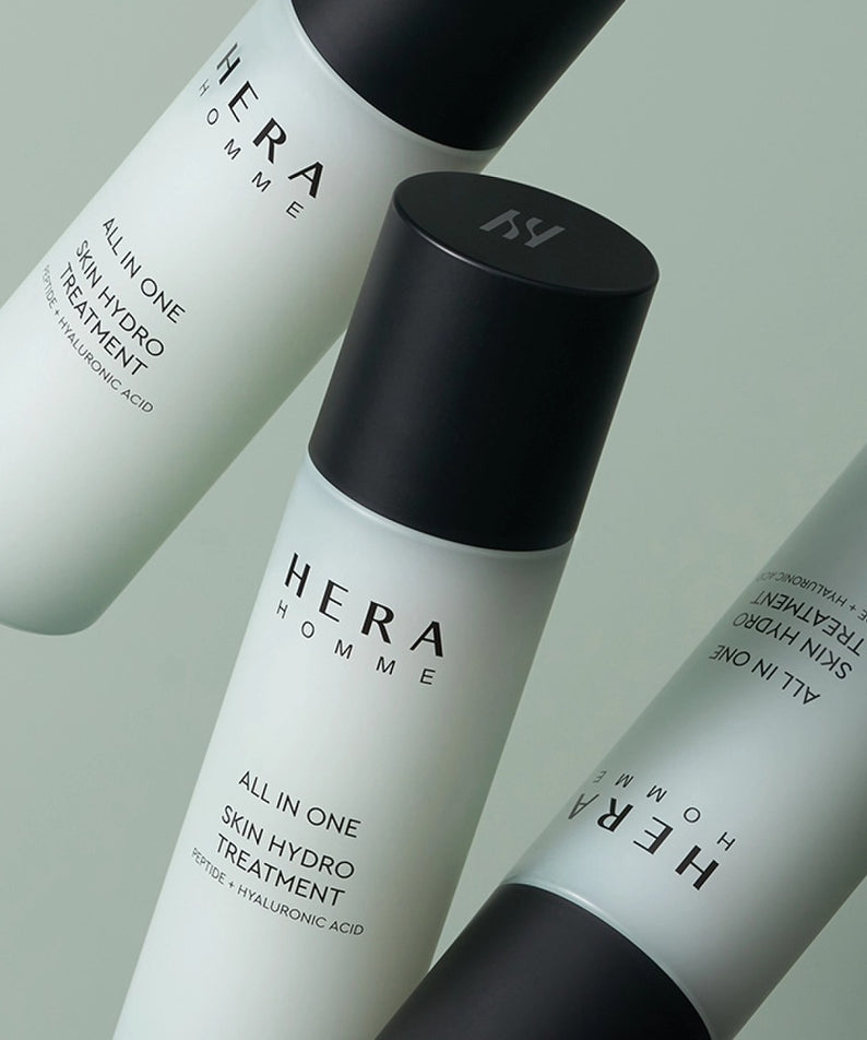 Trois bouteilles de HERA Homme All-in-One Skin Hydro Treatment 150ml sur fond vert.