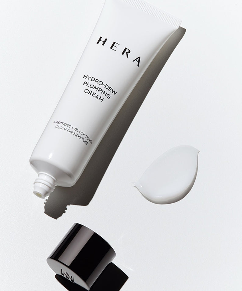 Tube de crème HERA Hydro-Dew Plumping Cream 50ml avec bouchon défait, vue d'un petit échantillon de crème à côté.