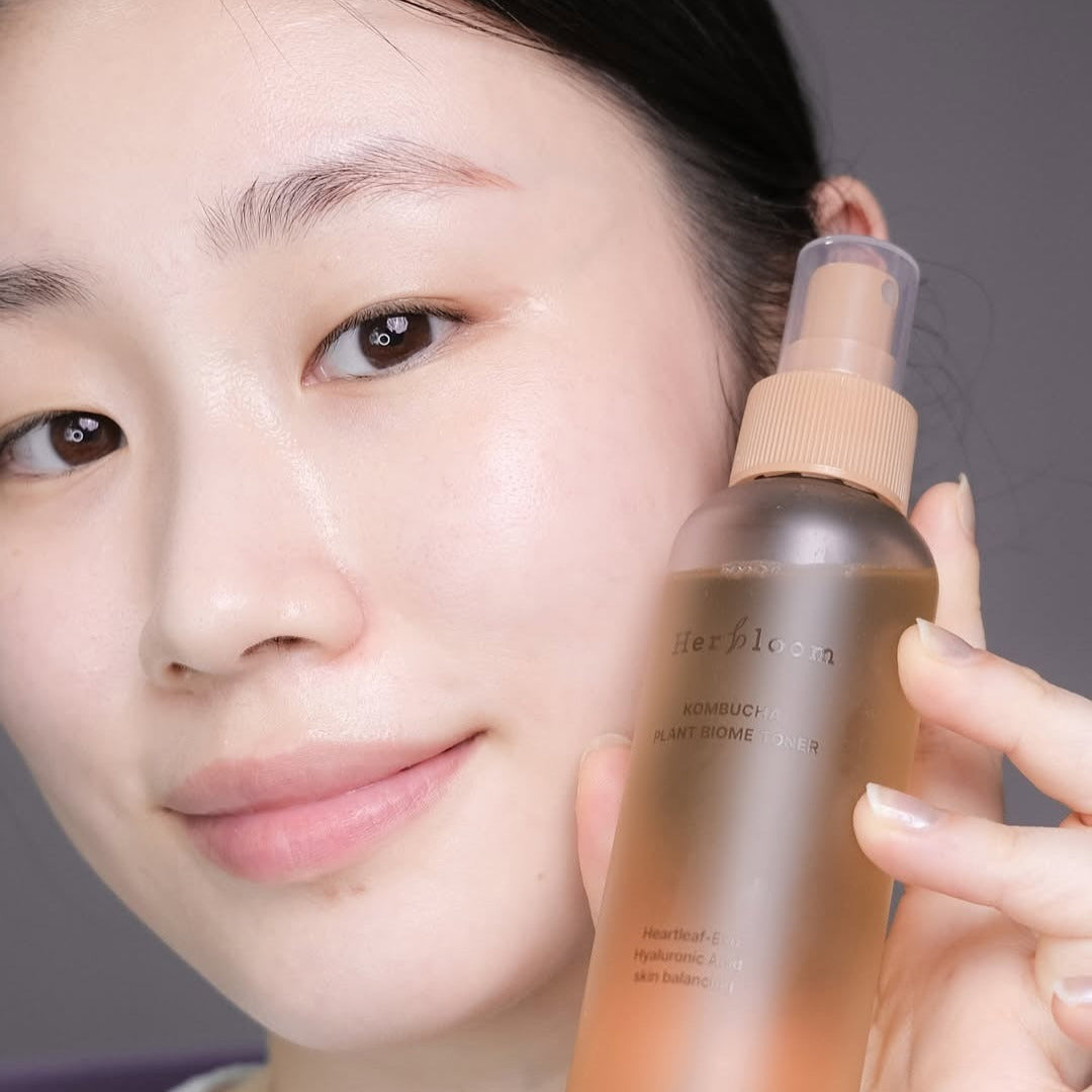 Décris l'image en français : HERBLOOM  Kombucha Plant Biome Toner 150g, femme tenant le flacon, visuel skincare en gros plan.