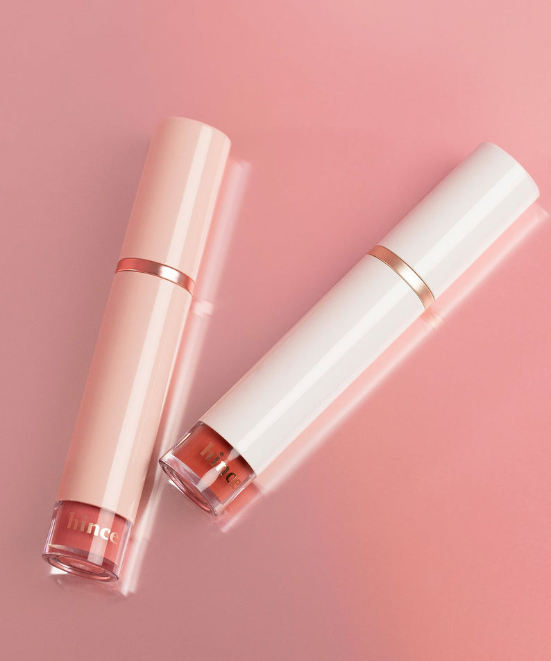 HINCE Mood Enhancer Water Liquid Glow sur fond rose, deux emballages élégants, rehausseur de teint et éclat liquide.