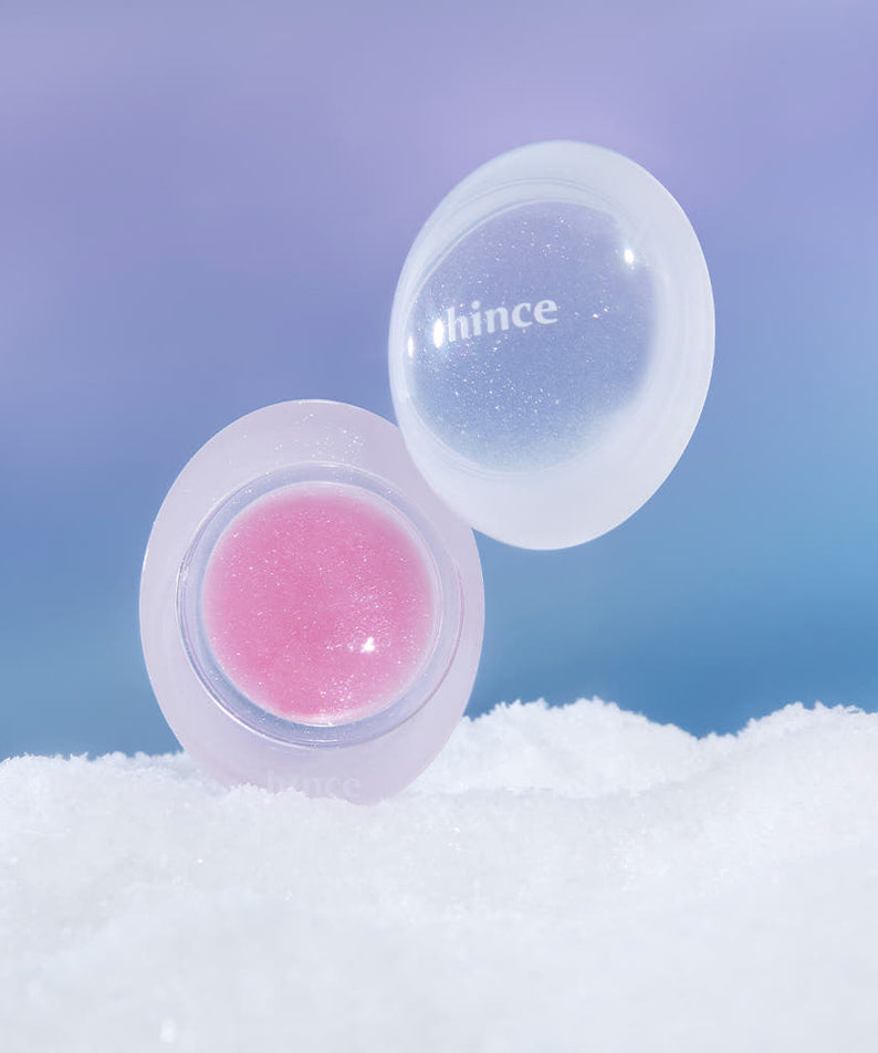 Produit cosmétique HINCE Low Glow Dewy Ball (Lip & Cheek) sur fond neigeux, design élégant et lumineux pour lèvres et joues.