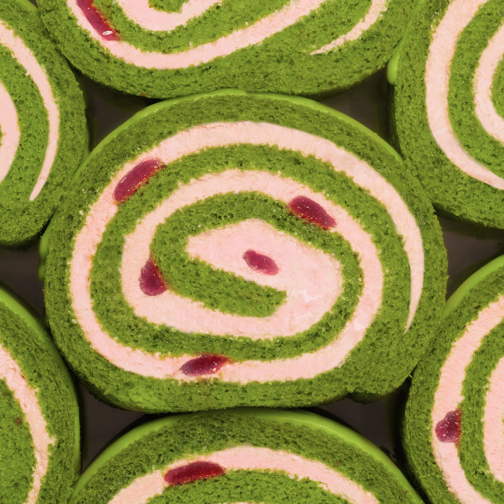 HIT THE TEA Super Matcha Strawberry Rool Cake Gluten-Free : tranches en spirales vert matcha et rose, fond chocolat noir.