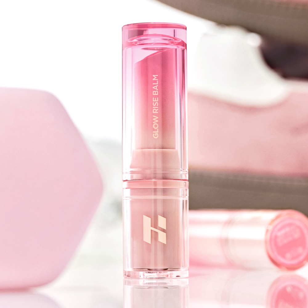 HOLIKA HOLIKA Glow Rise Balm, stick baume rose translucide sur fond doux rose et blanc, gros plan produit de la marque.