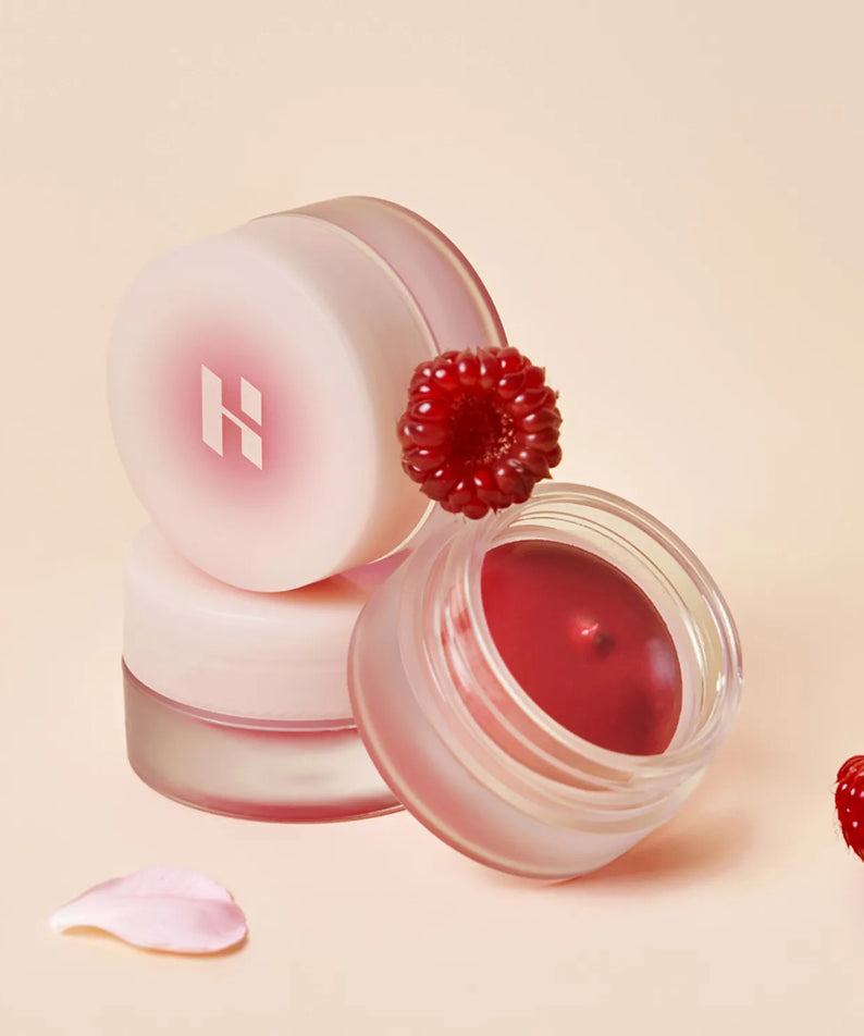 HOLIKA HOLIKA Melting Blur Lip Pot 5g, baume pour les lèvres crémeux, présenté avec des framboises, sur fond rose.
