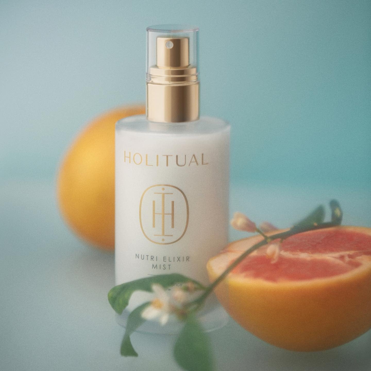 HOLITUAL Elixir Mist 140ml, brume visage en flacon doré sur fond bleu avec agrumes et fleurs, beauté