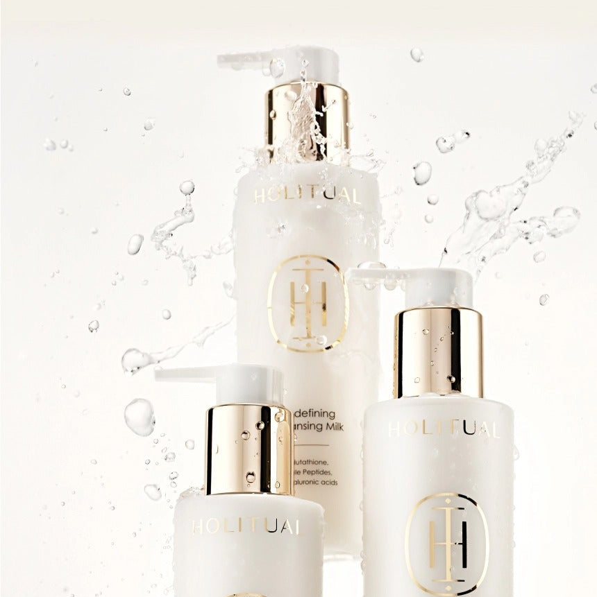 HOLITUAL Redefining acleansing Milk 200ml, flacon blanc et or sur fond crème avec éclaboussures d’eau, marque HOLITUAL