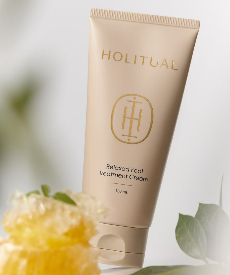 Crème pour les pieds HOLITUAL Relaxed Foot Treatment Cream 130ml en tube beige avec plantes en fond.