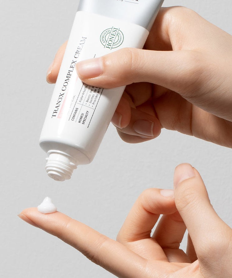 HONESI  Tranex Complex Cream 50ml, main appliquant la crème sur la peau, flacon blanc HONESI sur fond clair.