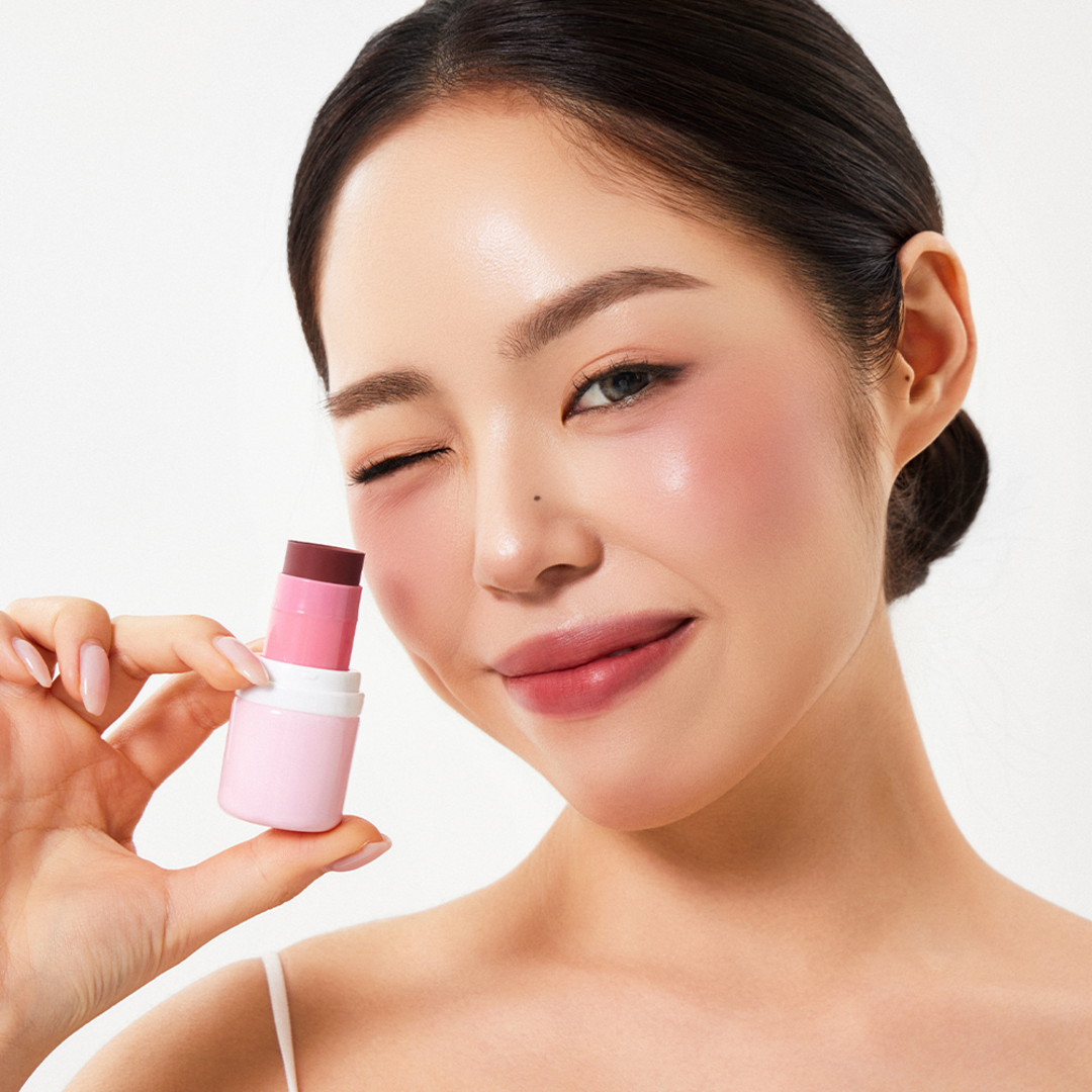 HOUSE OF HUR Every Cheek Blush de la marque, sur peau maquillée : modèle tient le blush rose en studio fond clair.