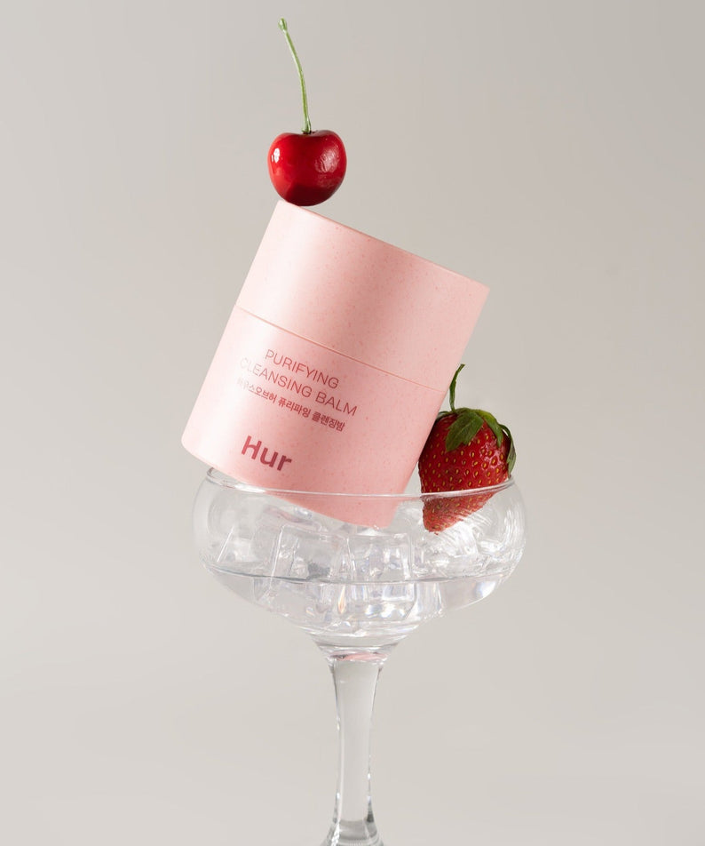 "Produit HOUSE OF HUR Purifying Cleansing Balm avec cerise et fraise, packaging rose dans un verre à martini."