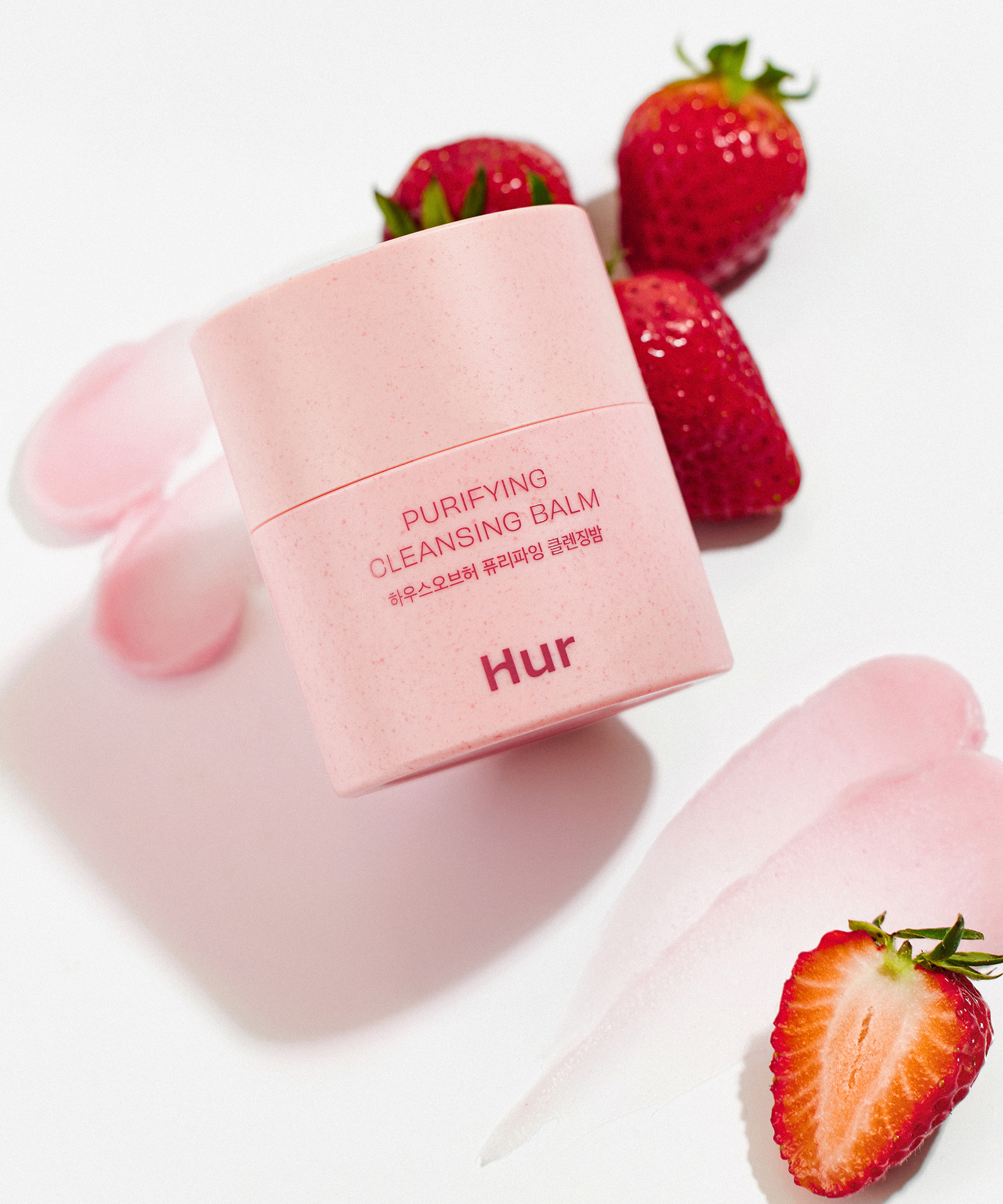 HOUSE OF HUR Purifying Cleansing Balm accompagné de fraises fraîches et de traces de baume rose sur fond blanc.