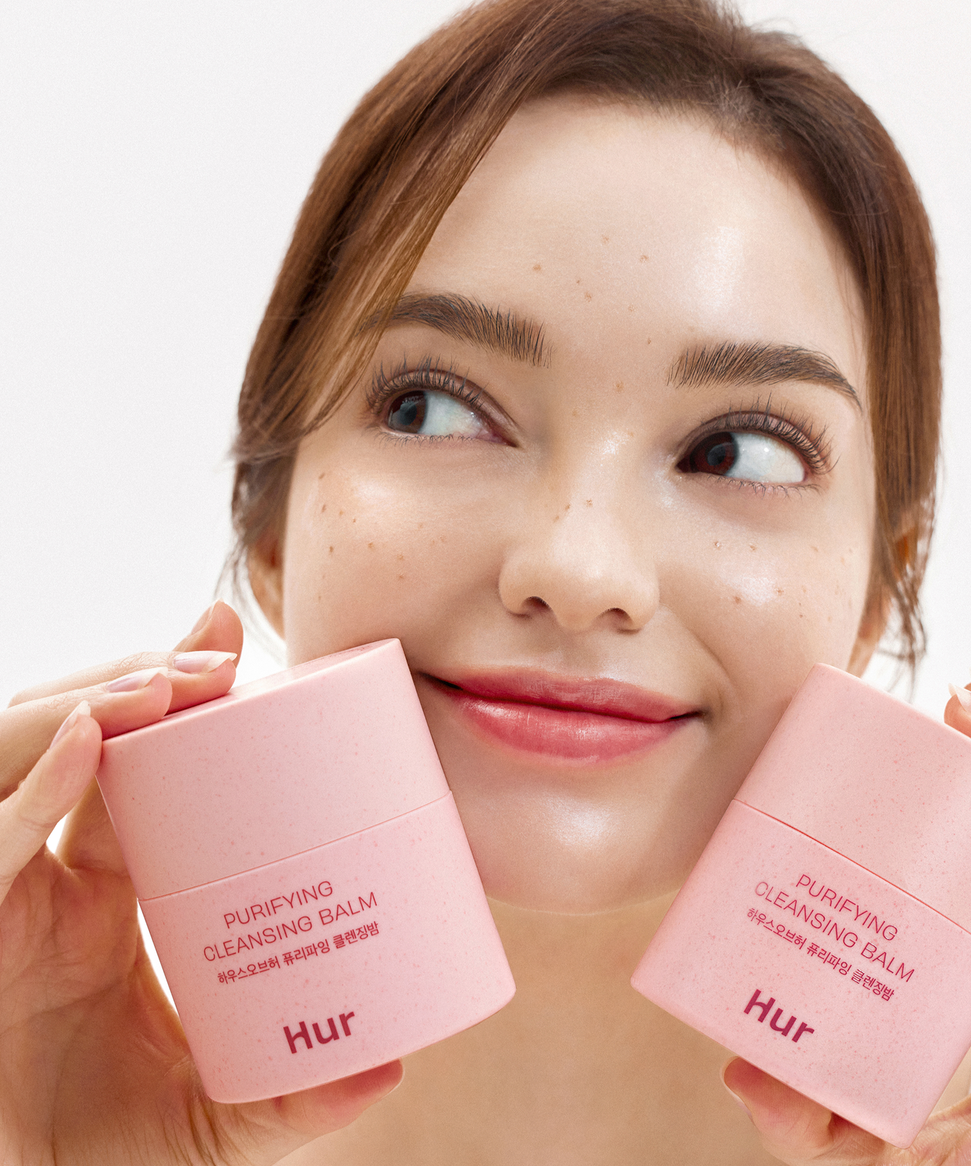 Femme souriante présentant le HOUSE OF HUR Purifying Cleansing Balm, baume nettoyant purifiant pour une peau éclatante.