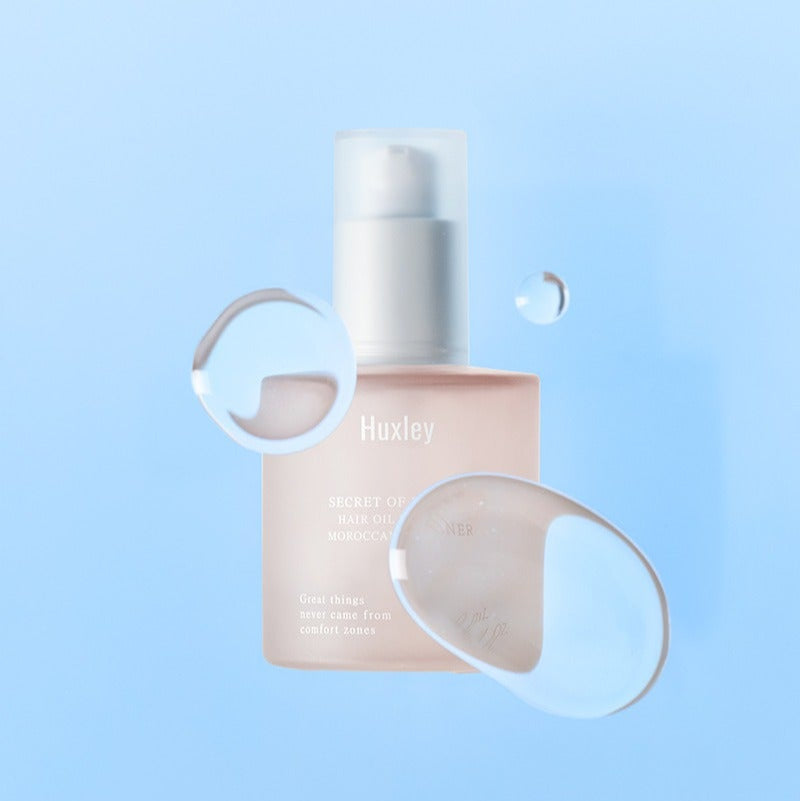 Décris l'image en français : HUXLEY Hair Oil Essence Moroccan Gardener 50ml, flacon Huxley sur fond bleu clair, goutte d'huile.