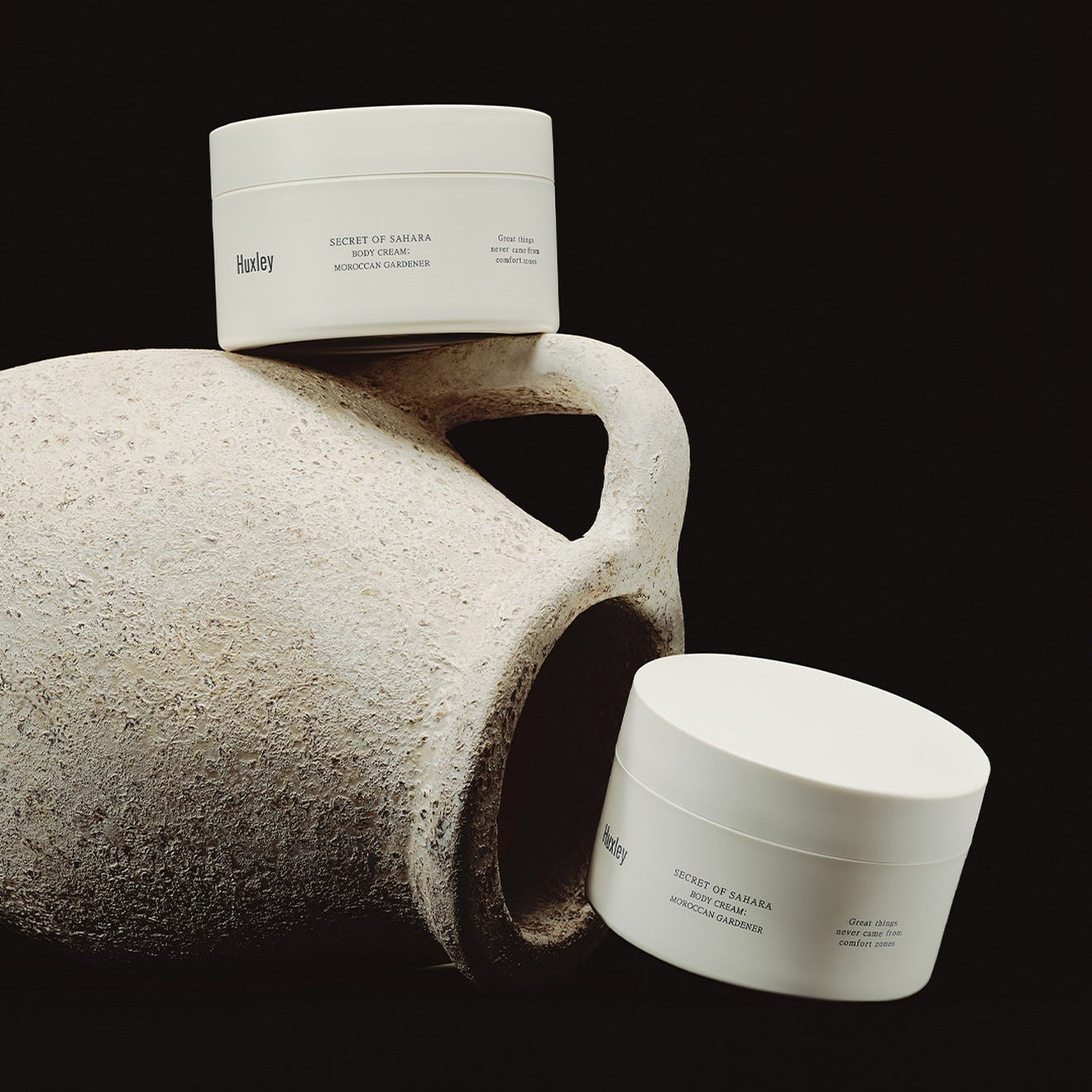 HUXLEY Moroccan Gardener Body Cream 200ml : pot blanc sur galet gris, fond sombre, marque Huxley, contexte spa.
