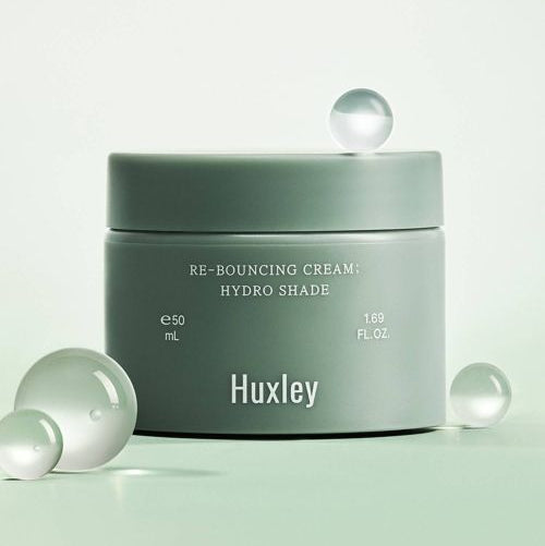 HUXLEY Rebouncing Cream Hydro Shade 50ml, pot vert sur fond clair, sphères décoratives, branding Huxley.