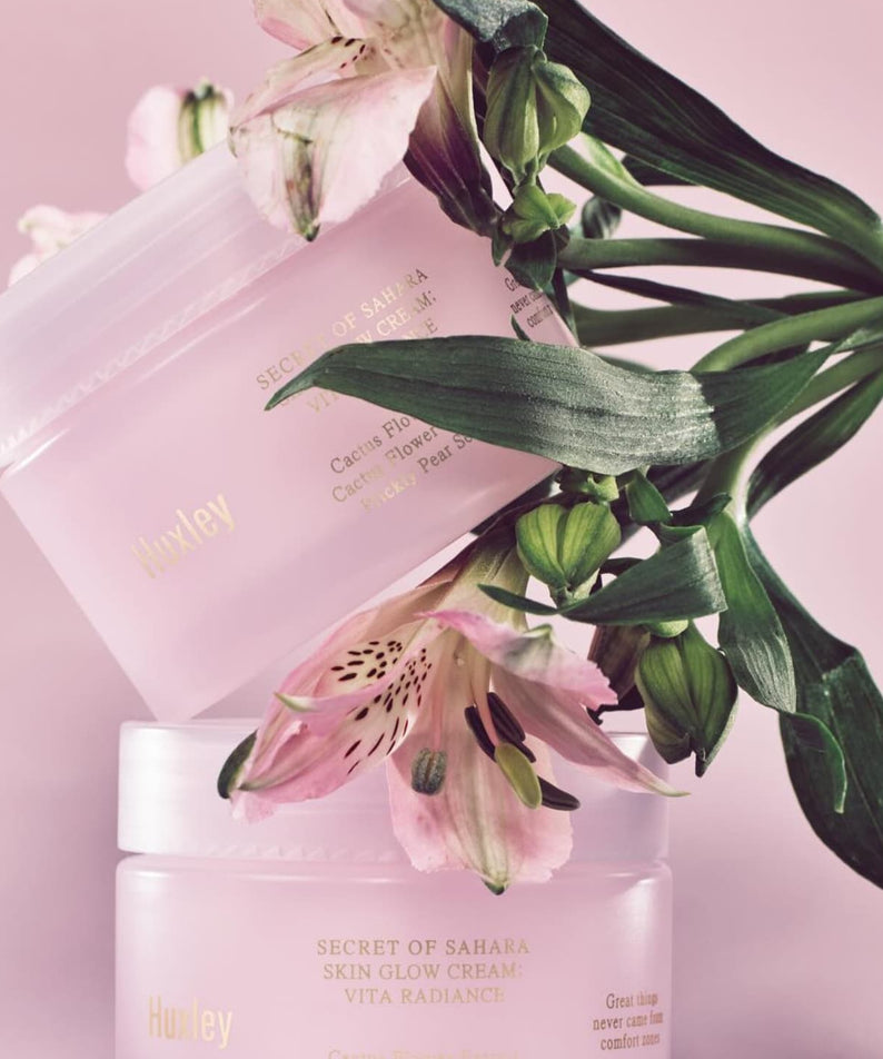 Crème éclat peau HUXLEY Skin Glow Cream Vita Radiance avec fleur rose sur fond pastel.