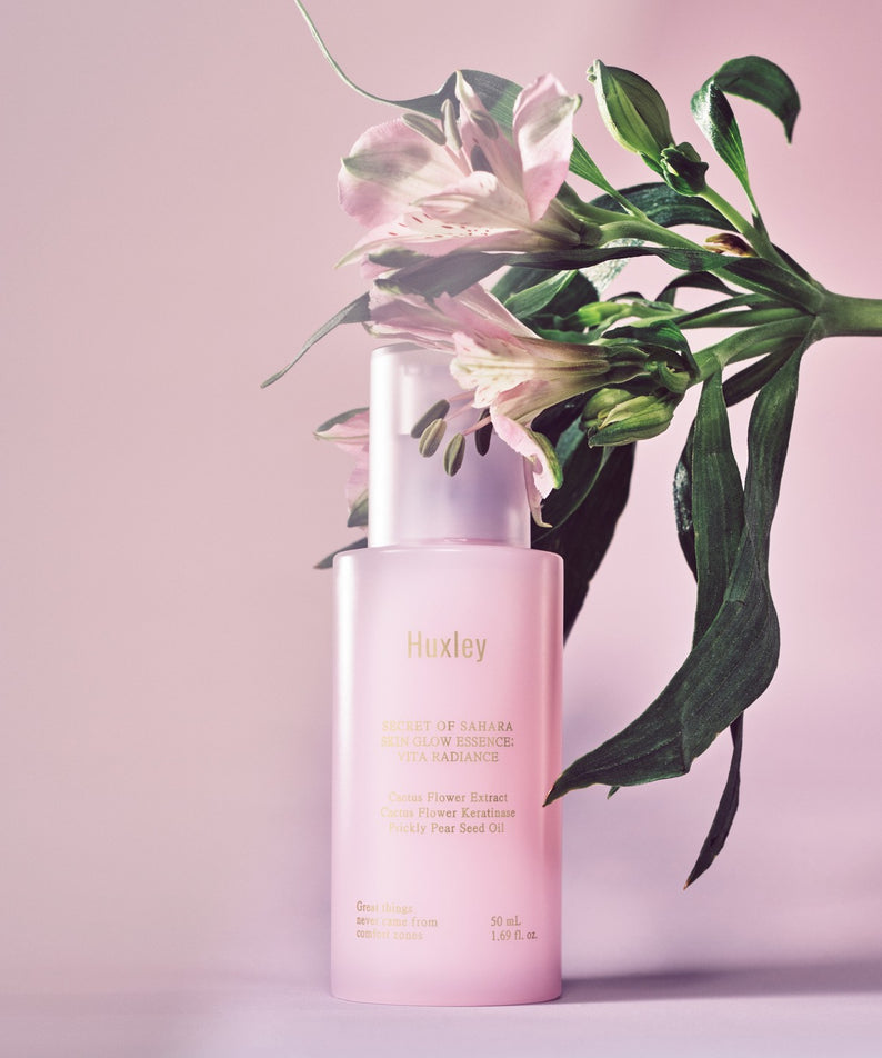HUXLEY Skin Glow Essence Vita Radiance avec fleurs et arrière-plan rose