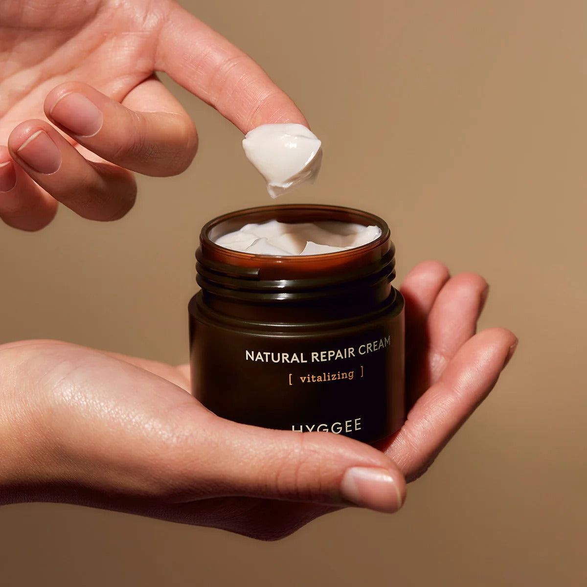 HYGGEE Nature Repair Cream 50ml, crème en pot ouverte, mains appliquant une texture blanche, style beauté naturel