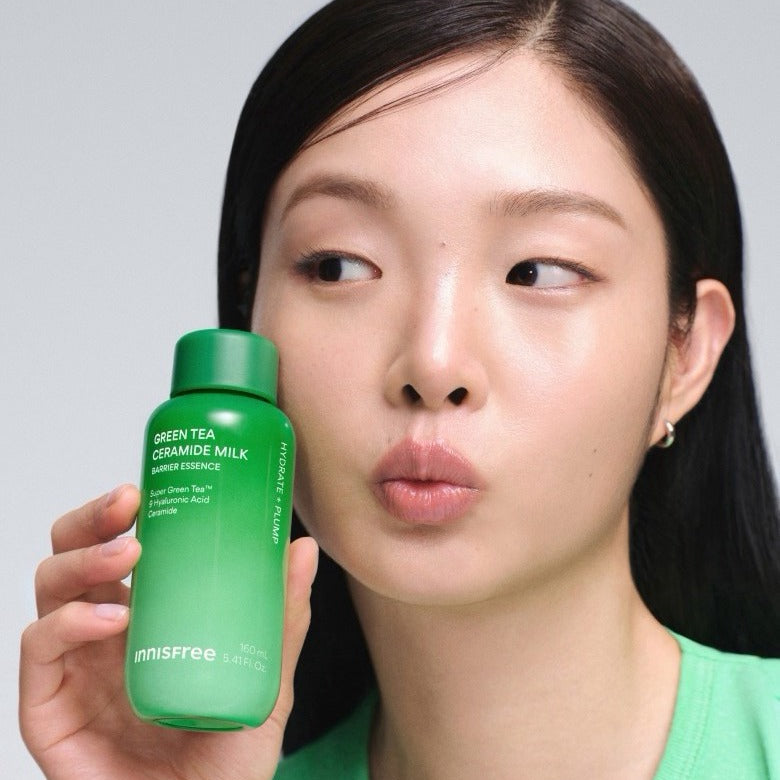 INNISFREE Green Tea Ceramide Milk Essence 160ml, flacon vert tenu par une femme au maquillage minimal, fond clair.
