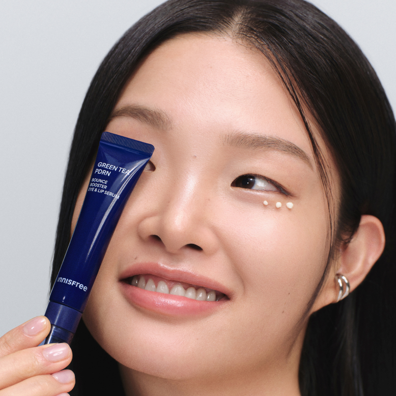 INNISFREE Green Tea PDRN Eye & Lip Serum 15ml : tube bleu appliqué près des yeux sur une femme, peau lumineuse, fond clair.