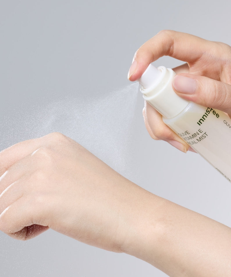 INNISFREE Olive Vitamin E Real Oil Mist 75ml, main vaporisant l’huile sur la peau, visuel beauté INNISFREE sur fond clair.