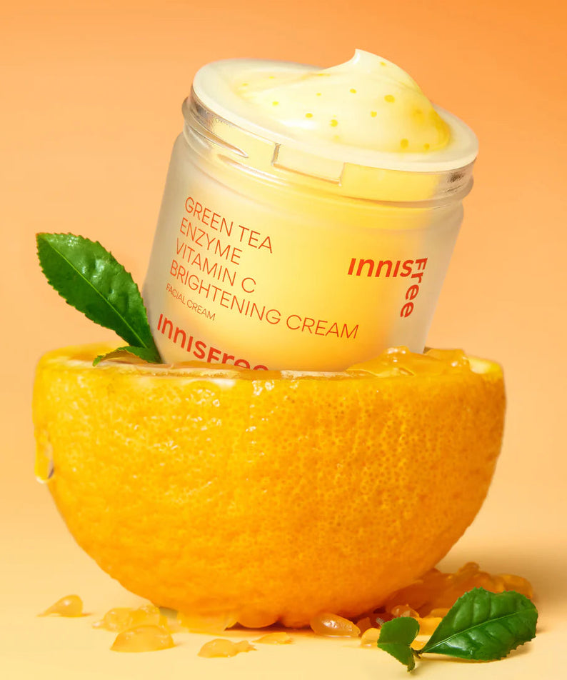 INNISFREE Vitamin C Enzyme Brightening Cream 50ml de la marque Innisfree, pot crème sur agrume et feuilles, fond orange.