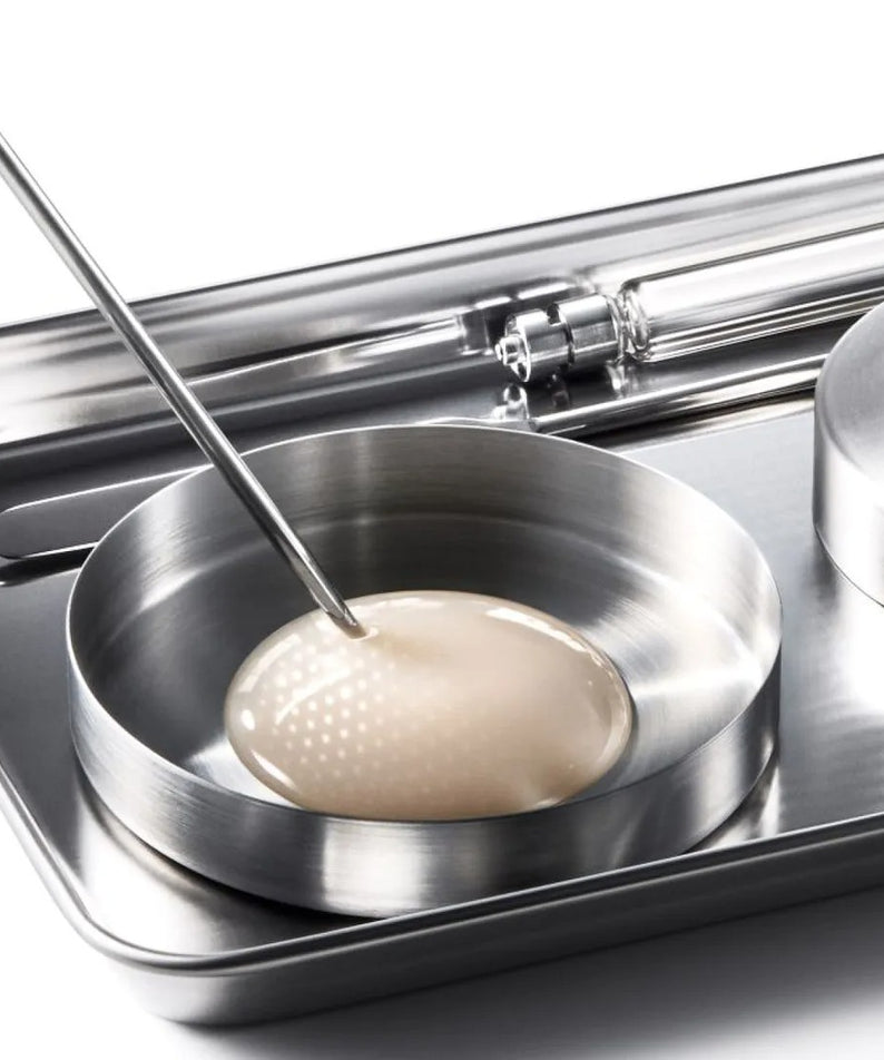 Décris l'image en français : IOPE XMD Stem3 Clinic Recoery Serum 50ml, fiole sur plateau clinique inox, ambiance laboratoire.