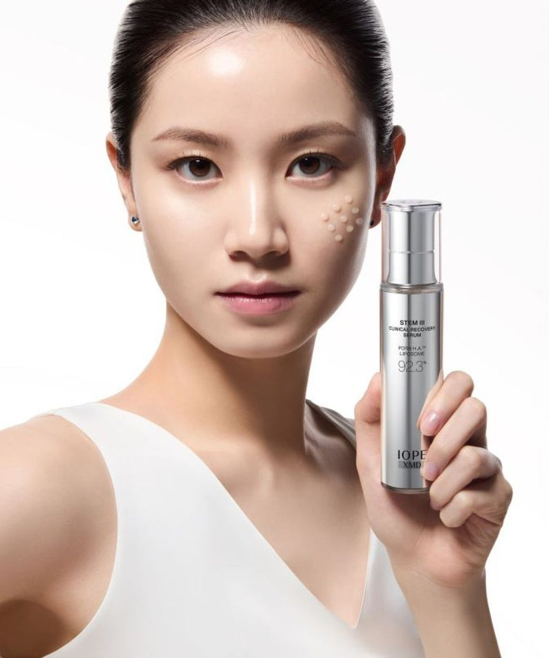 IOPE XMD Stem3 Clinic Recoery Serum 50ml : femme tenant le flacon, fond clair, marque IOPE, contexte skincare.