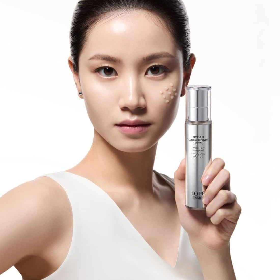 IOPE XMD Stem3 Clinic Recoery Serum 50ml : femme tenant le flacon, fond clair, marque IOPE, contexte skincare.