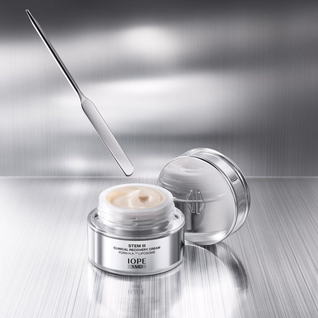 IOPE XMD Stem3 Clinical Recovery Cream 50ml, pot crème et couvercle ouverts sur fond métallique, vue produit en gros plan.