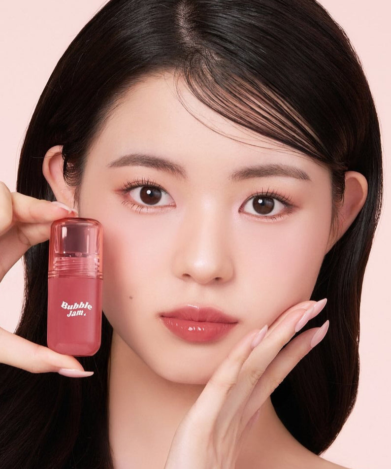 IPKN Bubble Jam Gloss : flacon rose tenu par un mannequin, maquillage lèvres brillantes, fond rose pastel.