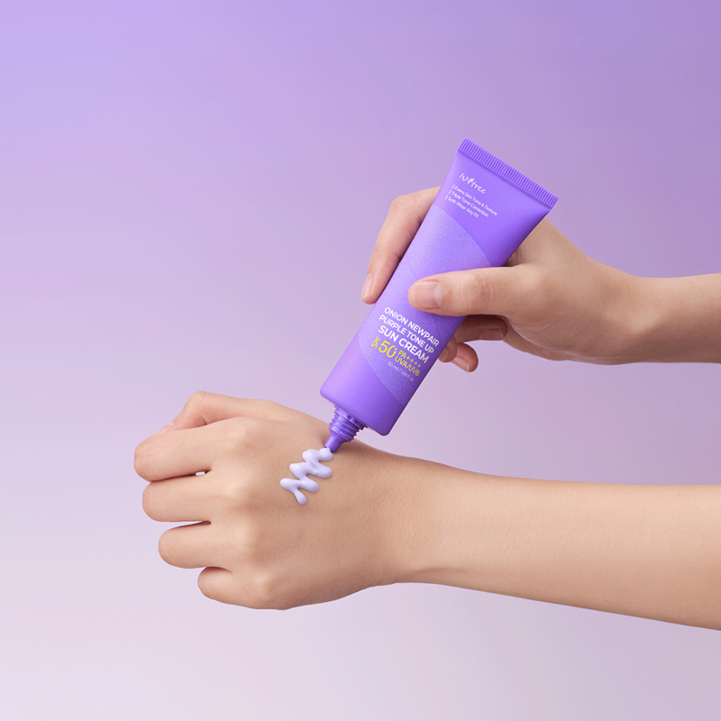 ISNTREE Onion Newpair Purple Tone-Up Sunscreen 50ml, main appliquant une crème violette sur la peau, fond violet.