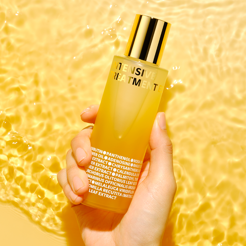 IS0I Intensive Treatment Essence 130ml ISOI, flacon doré tenu main sur fond jaune lumineux, soin visage.