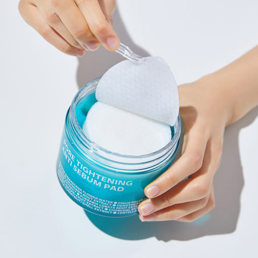 Main tenant ISOI Pore Tightening Anti-Sebum Pads 60 Sheets, pads appliqués sur peau, contexte beauté/soin visuel.