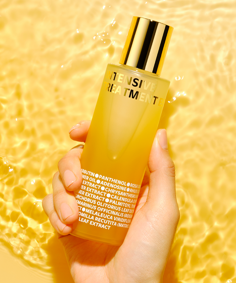 Flacon de ISOI Intensive Treatment Essence 130ml tenu dans une main sur fond jaune, offrant soin intensif et hydratation.