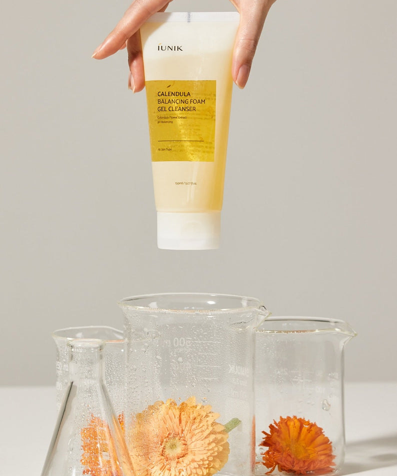 IUNIK Calendula Balancing Foam Gel Cleanser 150ml, flacon tenu en main, fleurs de calendula sur fond clair