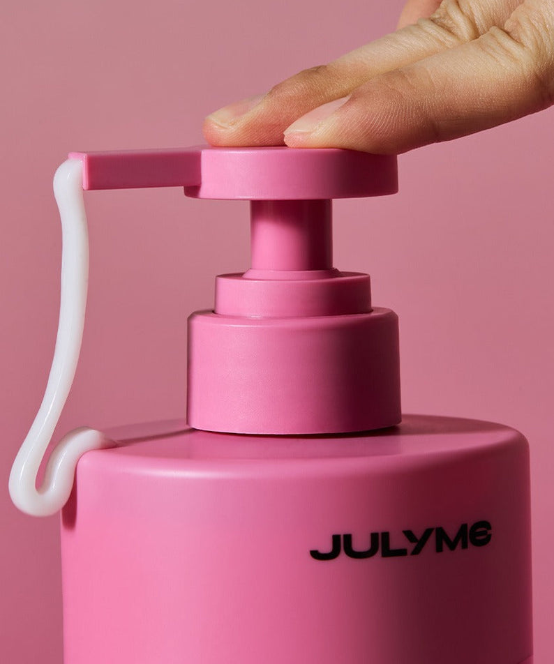 Main ouvre JULYME Damage Care Perfume Hair Treatment 500ml, bouteille rose JULYME sur fond rose, soins capillaires