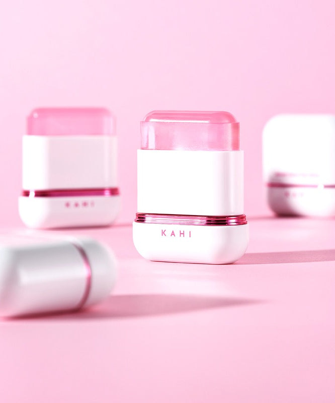 KAHI Velvet Glow Sun Stick 13.5g, stick solaire KAHI sur fond rose pastel, flacons cosmétiques en arrière-plan
