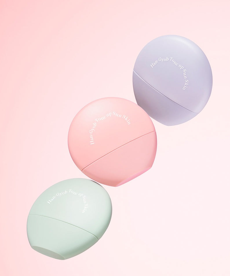 Trois flacons colorés de KAHI One Layer Tone-up Sun Skin 40ml sur fond rose, protection solaire et amélioration de teint.