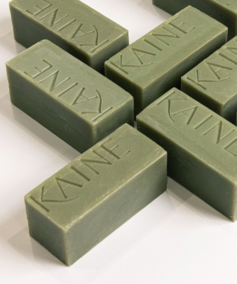 Barres de savon KAINE Rosemary Acne Mildly Acidic Cleansing Bar 100g disposées de manière esthétique sur une surface blanche.