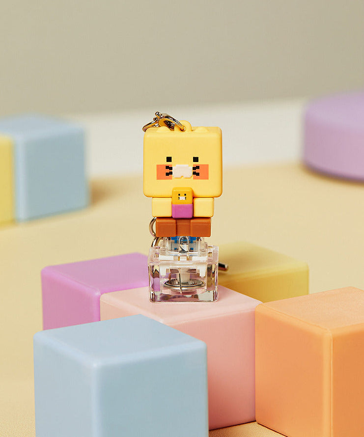 Décris l'image en français : KAKAO FRIENDS Chunmyami LED keycap figure keyring, porte-clés lumineux sur blocs pastel.