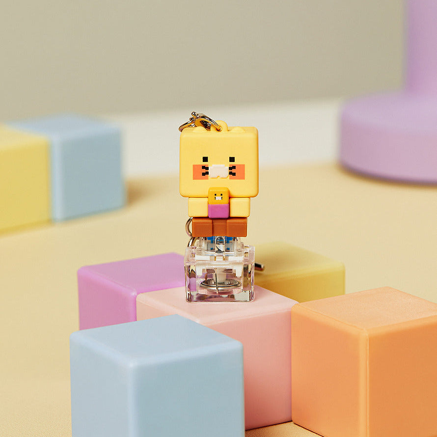 Décris l'image en français : KAKAO FRIENDS Chunmyami LED keycap figure keyring, porte-clés lumineux sur blocs pastel.