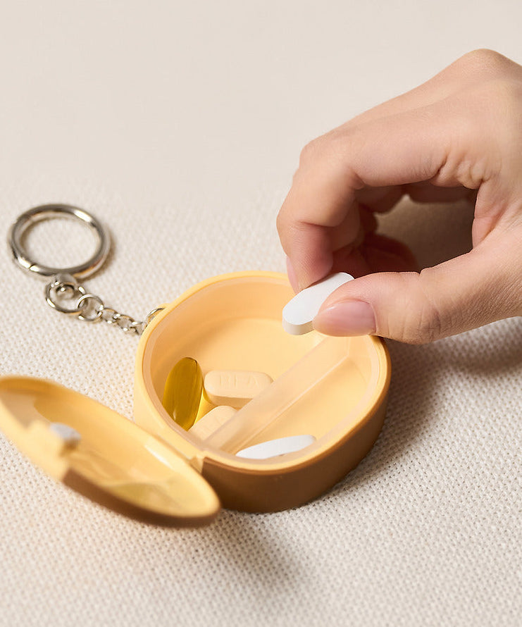 Décris l'image en français : KAKAO FRIENDS Medicine bottle keychain, mini pilulier, main ouvre le porte-clés sur fond clair.