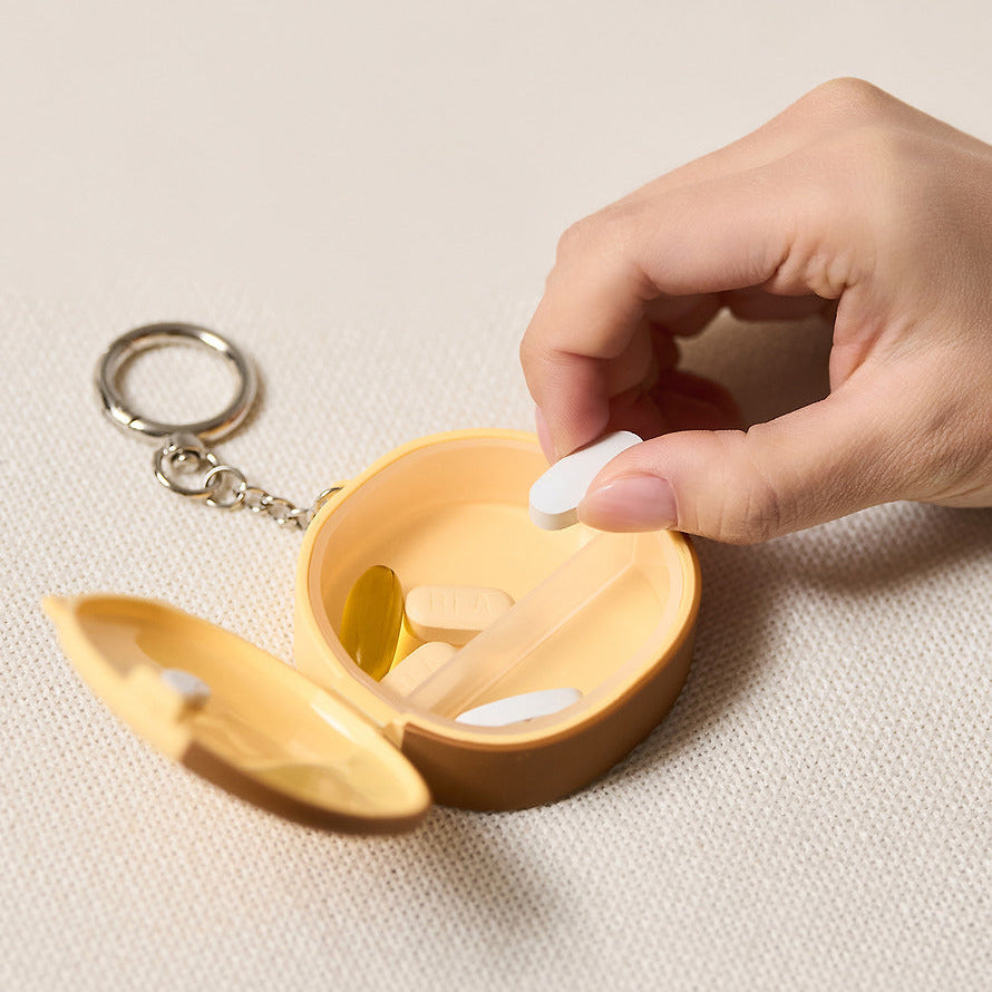Décris l'image en français : KAKAO FRIENDS Medicine bottle keychain, mini pilulier, main ouvre le porte-clés sur fond clair.